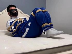 Young Asian man in hogtie bondage with a blindfold and a tape gag